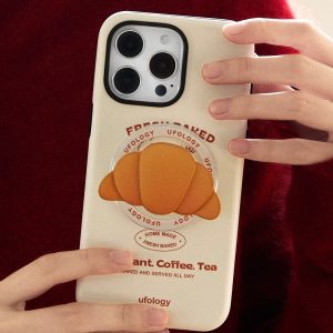 Hands holding the cream bakery-print case against a deep red sweater