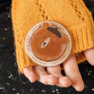 Open hand holding the beret bear grip in front of a mustard knit sleeve