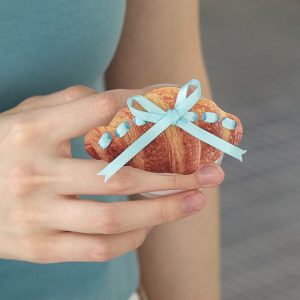 Hand holding the croissant bow grip against a teal top