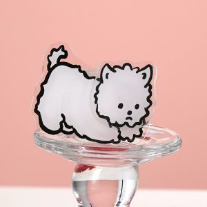 Fluffy dog grip standing on a glass candle holder against a pink wall