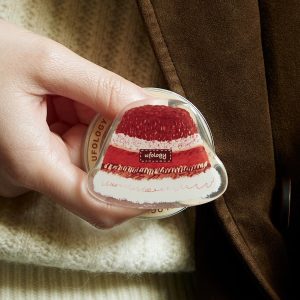 Hand holding the red velvet cake grip against a cream sweater